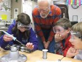 Three students wearing goggles doing an experiment with their teacher.
